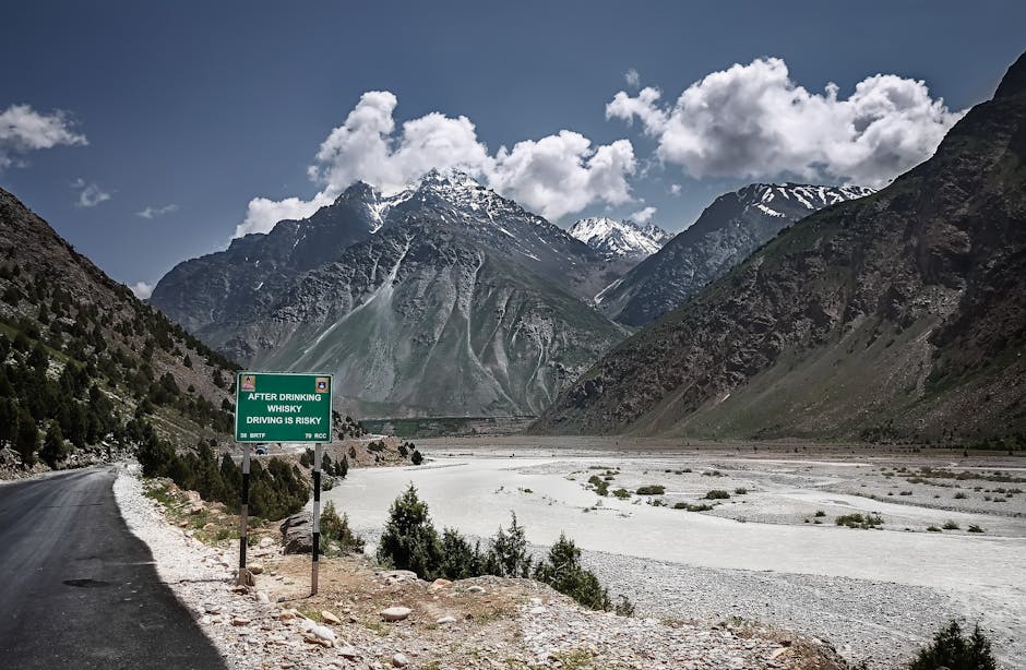 Mountain road with a safety sign against stunning snow-capped peaks and clouds.